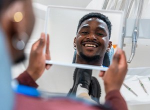 a man looking at his smile in a mirror at the dental office