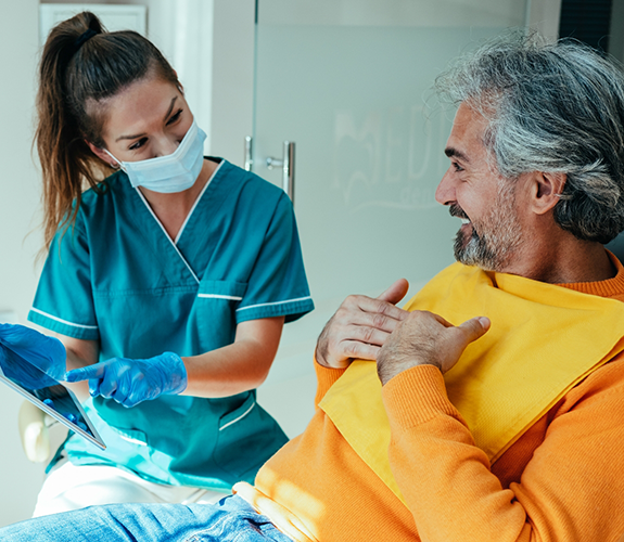 Dental team member showing a tablet to an older man in the dental chair