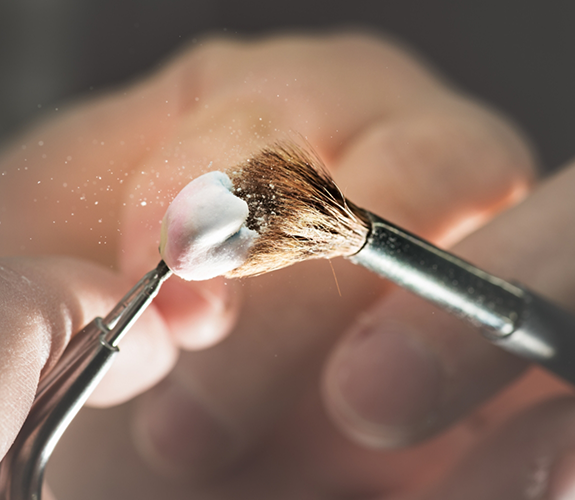 Dental professional adjusting a dental crown with a small brush