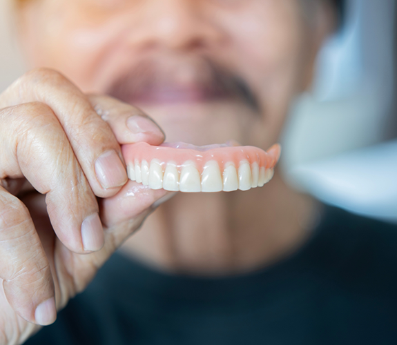 Man holding a full upper denture in front of his face