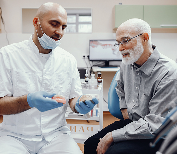 Dentist showing a set of dentures to a senior male patient