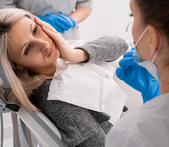 Woman in dental chair holding the side of her face in pain