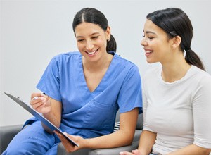 Dental assistant reviewing information on clipboard with smiling patient