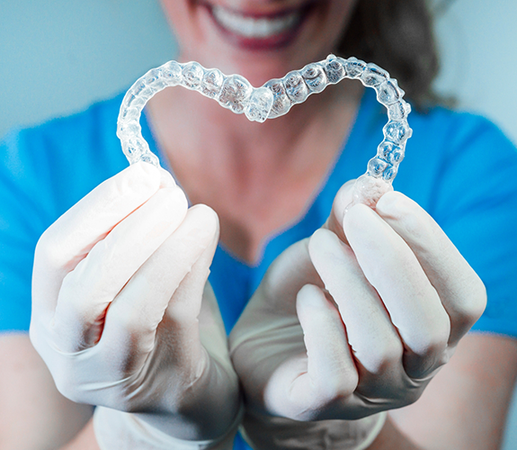 Dental professional holding two Invisalign trays in the shape of a heart