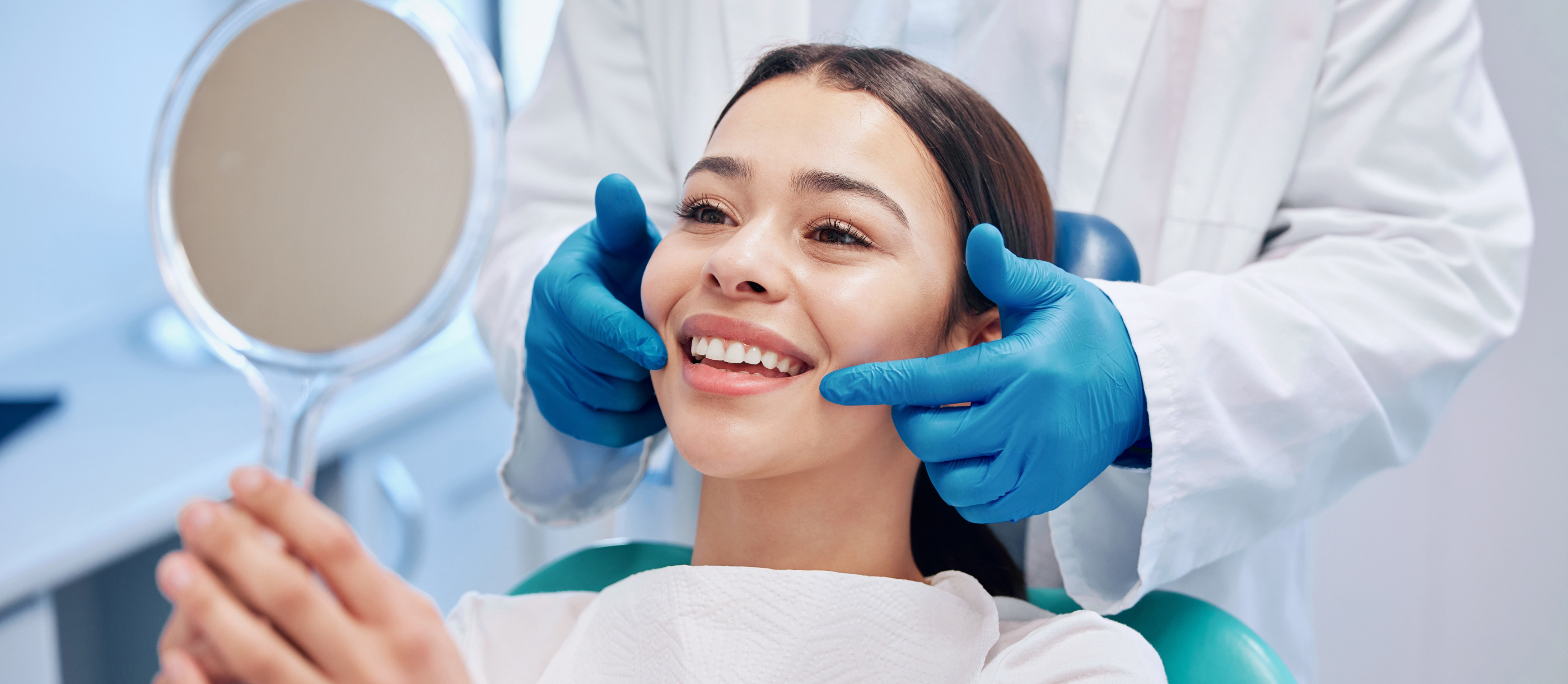 Dental patient admiring her smile in a mirror after replacing missing teeth in Boynton Beach