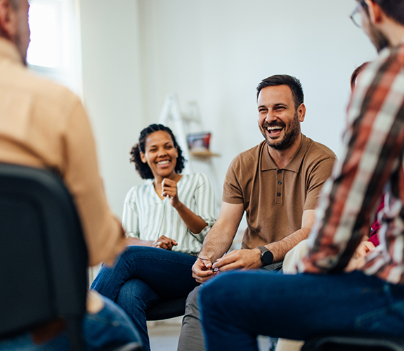 Group of smiling adults sitting in a circle of chairs