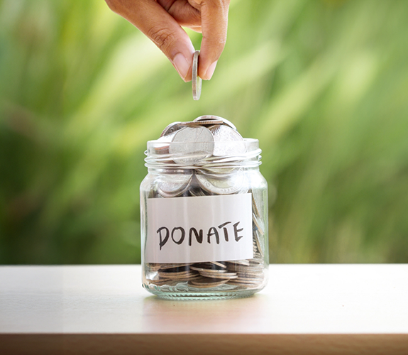 Hand placing a coin in a glass chair labeled donations