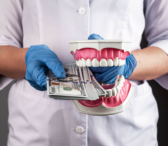 Dentist holding a model of the teeth and several hundred dollar bills