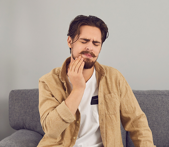 Young man wincing in pain and holding his cheek