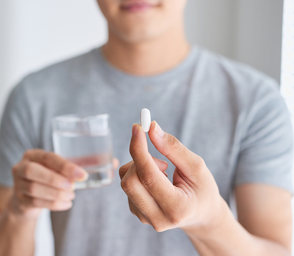 Person holding a white pill and a glass of water