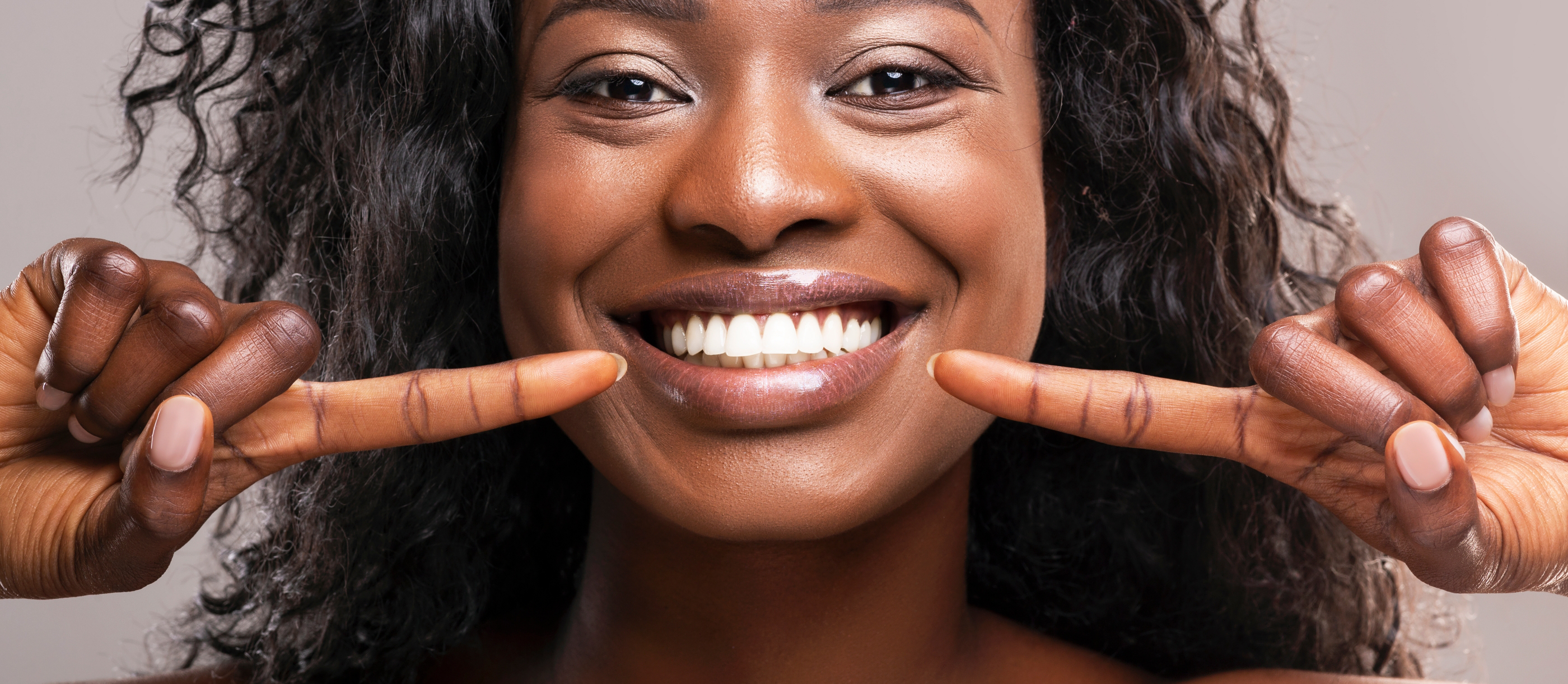 Woman pointing to her bright smile after teeth whitening in Boynton Beach