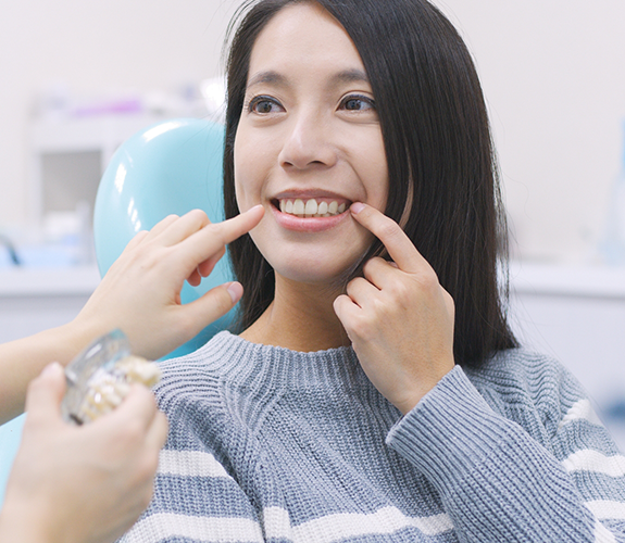 Young woman in dental chair pointing to her smile