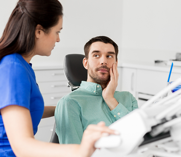 Man in dental chair holding his cheek while looking at his dentist