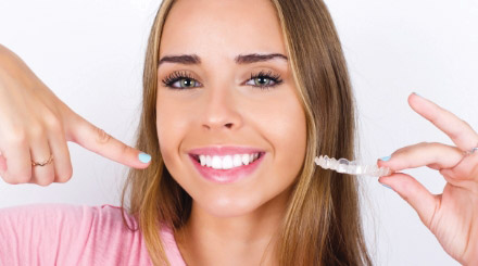 woman-holding-invisalign-clear-aligners-while-pointing-at-her-mouth